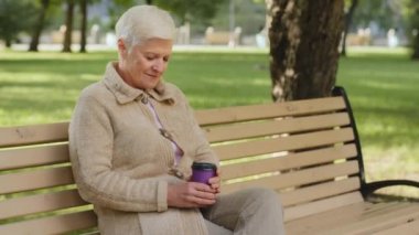 Rüya gibi sakin, gri saçlı yaşlı büyükanne parkta bankta oturmuş bardaktan kahve içiyor. Emeklilik yaşında, şık, çekici, olgun bir kadın. Günlük kıyafetleriyle açık havada eğleniyor.