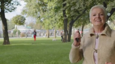 Modern kablosuz kulaklıklar takan neşeli, çekici, aktif bir emekli, enerjik melodiler dinleyen, akıllı telefon kullanan hoş bir müzik radyosu. Olgun kadın emeklilik yaşı dışarıda eğleniyor.
