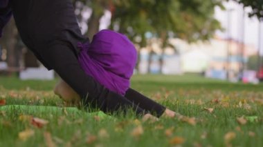 Güçlü genç bayan öğretmen yoga akışı egzersizi yapıyor. Sağlıklı vücut için asana otların üzerindeki enerjiyi hisset. Başörtüsü takmış köpek pozu veren kız parkta pratik yapıyor. Egzersiz yapan dikkatli Budist kadın.