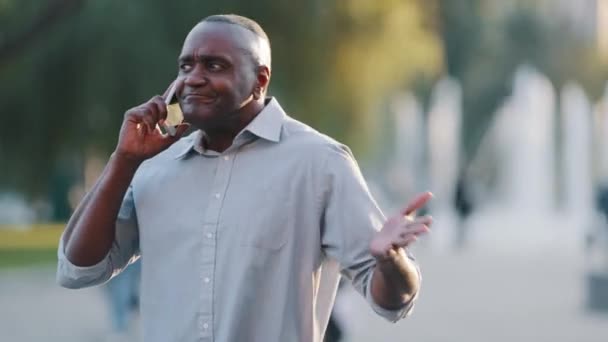 Förvirrad förvirrad förvirrad förvirrad mogen vuxen afroamerikansk pensionär står utomhus håller smartphone har svårigheter, svart man i pensionsåldern har frågor, gick vilse, behöver hjälp, förklaring — Stockvideo