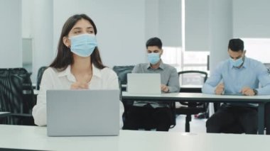 Modern ofiste çok ırklı çalışanlar dizüstü bilgisayarlarla ortak çalışma alanında oturuyorlar. Düşünceli kız işiyle meşgul. Yüz maskesi takın, mesafeyi koruyun, salgın hastalık nedeniyle kişisel güvenlik