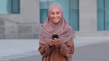 Müslüman genç kadın kullanıcı iş kadını portresi. Elinde cep telefonu olan pembe tesettürlü kız çocuğu. İnternet üzerinden gülen mesajlar yazmak için akıllı telefon kullanıyor.