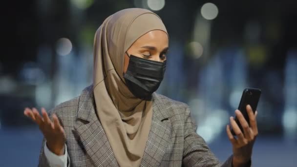 Açık havada çekilmiş kadın portresi İslami kadın tesettür ve tıbbi maske takıyor. Şehir merkezinde cep telefonu uygulaması, akıllı telefon blogcusu ve merhaba cep telefonu ile iş görüşmesi yapıyor. — Stok video