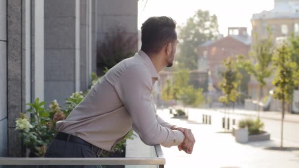Glad pensiv framgångsrik avslappnad affärsman latinamerikansk kille man arabiska investerare affärsman står på terrassen balkong i kontorsbyggnad i hotellrum hemma tänker titta på stadsbilden njuta av utsikten — Stockvideo