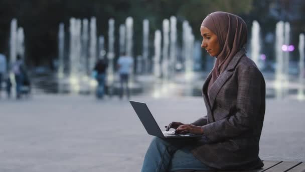 Jovem mulher de negócios muçulmano bem sucedido estudante islâmico menina usa hijab sentado na rua cidade ao ar livre fundo urbano digitando laptop trabalhando on-line e-learning fora com computador bate-papo aplicativo web — Vídeo de Stock