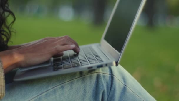 Närbild kvinnliga händer fingrar skriva på tangentbordet tangentbord bärbar dator text arbetar lärande e-lärande utomhus i parken. Oigenkännlig flicka brunett kvinna i jeans sitter på gräsmattan chatta online — Stockvideo