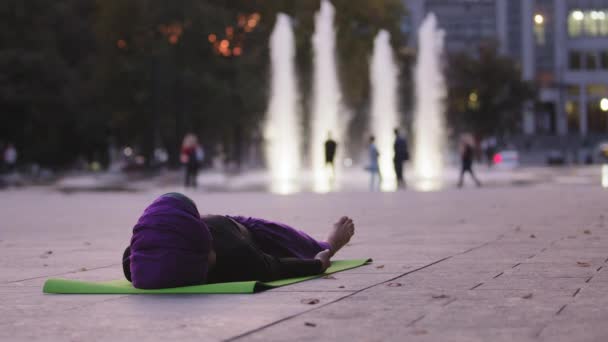 Muslimská islámská žena jóga dívka v hidžábu žena atlet unavená dáma leží na zelené podložce ve městě pozadí dělá savasana asana póza odpočinku relaxaci po jóga cvičení meditace venku ležící na zemi — Stock video