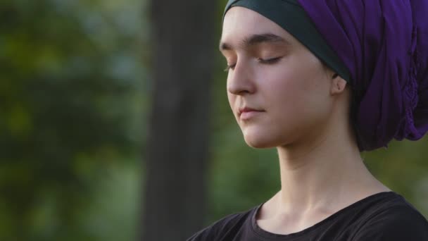 Beautiful young islamic woman girl muslim woman wears hijab outdoors, female calm face with closed eyes meditating breathes deep inhaling and exhaling air doing breathing exercises meditation in park — Stock Video