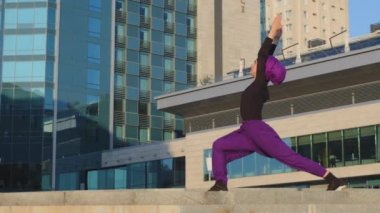 Tesettürlü aktif spor kadın güçlü kız antrenör Yogi modern binanın arka planında duruyor yoga egzersizleri yapıyor Asana savaşçı pozu veriyor sokakta meditasyon eğitimi veriyor.
