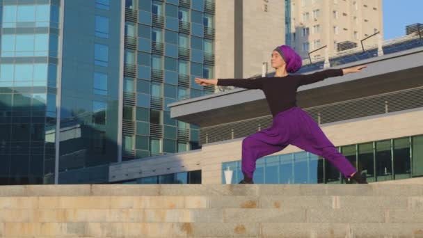 Sterke jonge kalme moslim islamitische vrouw in hijab meisje yogi sportvrouw dame vrouwelijke trainer doen yoga straat praktijk oefeningen buiten workout oefenen stad gebouw achtergrond strijder asana pose — Stockvideo