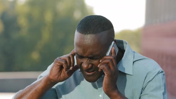 Serious angry Black Adult mature African American man sitting outdoors holding smartphone experiences difficulties with gadget need device repair dissatisfied with poor connection in roaming not hear — Stock Video