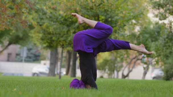 Ung stark sportig kvinna i hijab och lila byxor övning utomhus, flicka tränare gör stöds headstand hållning, yoga salamba sirshasana asana i parken på sommaren står på huvudet på gräs — Stockvideo