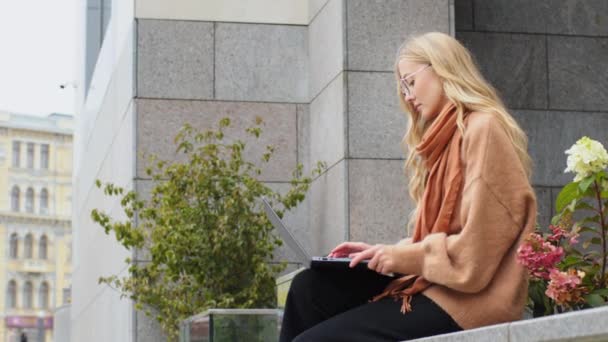 Успішна бізнес-леді, що сидить на вулиці біля будівництва кавказької молодої дівчини, яка навчається онлайн на відкритому повітрі, працює фрілансером, використовує бездротовий комп'ютер, друкуючи в міській леді балачки з клієнтом — стокове відео