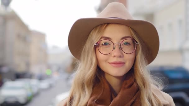 Portret pozytywna młoda kobieta z naturalnym makijażem atrakcyjny biały millenium ładna dziewczyna patrząc na aparat zbliżenie kobieta z długimi blond włosami uśmiech na ulicy pani w okularach i kapeluszu na zewnątrz — Wideo stockowe