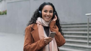 Güzel, mutlu, kaygısız, esmer bir kız şehirde yürüyen genç bir bayan. Cep telefonu kulaklıkları ile müzik dinliyor.