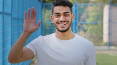 Çekici Orta Doğu Hindistanlı genç erkek sporcu spor kıyafetleriyle stadyumda el sallayarak yeni sporcuları selamlıyor, Arap sporcu aktif yaşam tarzını tanıtan takıma davet ediyor.