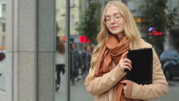 Επιτυχημένη νεαρή κοπέλα σταθεί στην πόλη κρατώντας φάκελο με έγγραφα των επιχειρήσεων γυναίκα ευτυχισμένο χαμόγελο κοιτάζοντας κάμερα επιχειρηματίας στο δρόμο περιμένει όμορφη κυρία πελάτη σε γυαλιά με μακριά ξανθά μαλλιά — Αρχείο Βίντεο