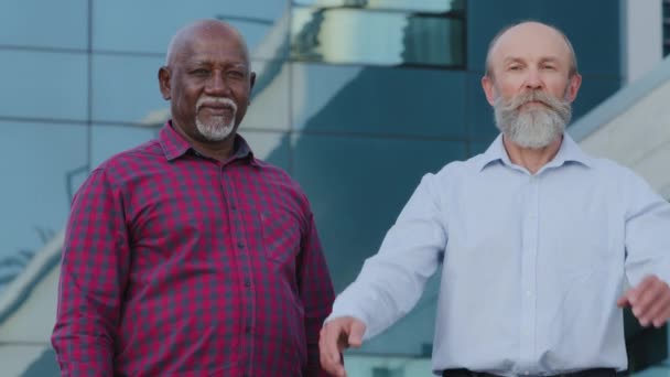 Retrato grave pareja madura diversa ancianos africanos y caucásicos hombres de negocios profesionales colegas de pie con los brazos cruzados al aire libre. Amistad a largo plazo, concepto de asociación segura — Vídeo de stock