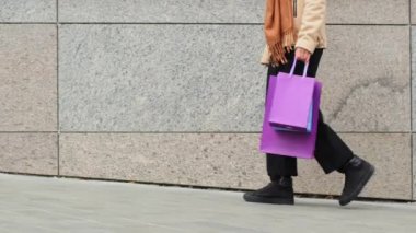 Sokakta tanınmayan genç bir kız siyah pantolonlu kadın bacakları ve ayakkabı tüketicisi kadın kaldırım boyunca yürüdükten sonra siyah cuma günü parlak alışveriş çantaları taşıyor.