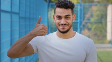 Neşeli Ortadoğu Arapça öğrencisi. Başparmak kaldırıyor, sembol onayı veriyor, destek veriyor. Yazın spor giyim kuşamında mutlu erkek sporcu iyimser, neşeli, başarıyı kutlayan, zafer, mükemmel sonuç