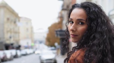 Kadın portresi güzel Latin kadın omzunun üstünden bakıyor esmer kız model turist şehir arka planında dikiliyor dişlek dişli dişçi gibi gülümseyen kameraya bakıyor.