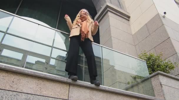 Spodní pohled mladá studentka tanec na balkóně terasa atraktivní tisíciletá dívka úsměv aktivně pohybovat šťastný kavkazský blond venku těší tanec úspěšný obchod žena stojí v blízkosti budovy — Stock video