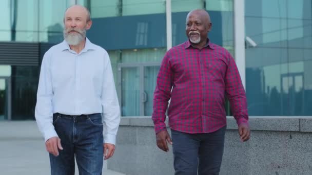 Homem caucasiano europeu idoso com barba cinza encontra velho amigo africano ou colega tem conversa interessante, mostra vistas, edifício de escritório moderno. Dois funcionários diversos têm um bom tempo juntos — Vídeo de Stock