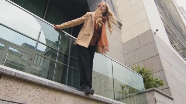 Vista inferior elegante hermosa joven pie en la terraza cerca de edificio de oficinas pensativa mujer se inclinó hacia adelante y levantar la cabeza hasta la celebración de carril de balcón mujer de negocios caucásica disfrutando del descanso al aire libre — Vídeos de Stock