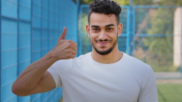 Alegre estudante árabe do Oriente Médio contente mostrando polegares para cima, aprovação de símbolo, apoio. Atleta masculino feliz no verão sportswear otimista, alegre, celebrando o sucesso, vitória, excelente resultado — Vídeo de Stock