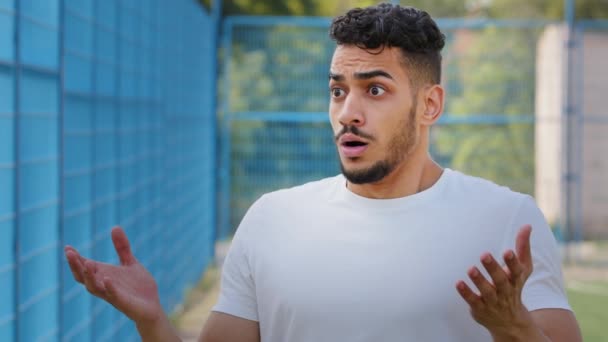Boję się zaskoczony oburzony arabski sportowiec w letni sportowy odzież gorączkowo gestykuluję wyrażenie niezadowolenie, oburzenie i niezgoda. Indian millennial oburzony sytuacją na stadionie — Wideo stockowe