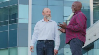 Çeşitli arkadaş canlısı erkek ortaklar ya da arkadaşlar dışarıda yürüyen yaşlı Afro-Amerikan ve Kafkasyalı iş adamları tatilde gülen ortak projeyi tartışıyorlar.