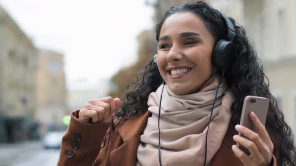 휴대 전화 헤드폰 이어폰으로 온라인 사운드 앱 오디오 mp3 노래를 즐기며 도시에 서 있는 행복 한 젊은 여성 관광객 브루 넷 여성 — 비디오