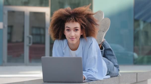 若いです学生の女の子アフリカ系アメリカ人のビジネス女性フリーランスユーザーのウェブデザイナーのマーケティング担当者小さな専門家は、屋外の通りに横たわっているオンラインで大丈夫なジェスチャーを示すノートパソコンのワーキングチャット学習を使用 — ストック動画