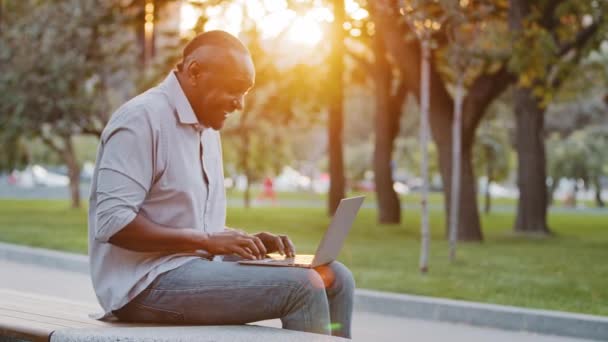 Cheerful carefree senior black man sitting outdoor using laptop, plays having fun laughing pretending to quickly type on computer like piano. African American mature male inspired by working on pc — Stock Video