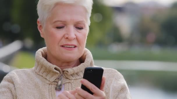클로즈업 회색 머리의 성숙 한 여성 현대 스마트폰 기기로 문자 메시지보내기, 스크롤, 터치 스크린, 놀랍게 도 할머니가 핸드폰으로 인터넷을 검색하기 , 온라인으로 명령을 내리는 동영상 — 비디오