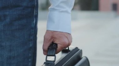 Yakından bir erkek eli, evrak çantalı bir işçi, tanınmayan modern yetişkin yetişkin yetişkin bir işadamı yaşlı bir işadamı ya da şehir sokaklarında deri çantayla gezen sıradan bir kot pantolon ve gömlek giyen bir profesör.