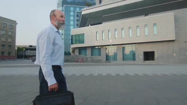 Hombre caucásico guapo de edad de jubilación en camisa casual y jeans Pensionista inteligente o profesor universitario barbudo paseando por la calle de la ciudad en viaje de negocios, caminando al departamento u oficina — Vídeo de stock