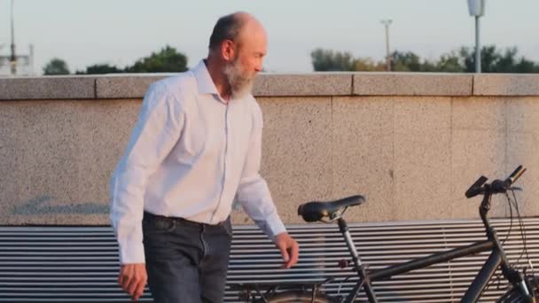 Pensionné âgé avec barbe grise se levant du banc monte sur son vélo moderne et s'en va. Gris-cheveux élégant grand-père de l'âge de la retraite homme âgé actif en vêtements décontractés chemise à l'extérieur — Video