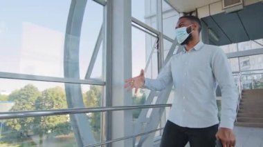 İki çok ırklı iş arkadaşı koruyucu tıbbi maskeler takarak ofiste buluşuyor. Afro-Amerikan erkeği, Coronavirus salgını sırasındaki güvenli tokalaşma selamlaması.