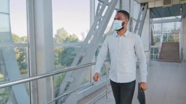 Dosyası olan başarılı Afro-Amerikan iş adamı ofiste yürürken tıbbi maske takıyor İspanyol meslektaşıyla karşılaşıyor ve Coronavirus salgını sırasında elini sıkıyor.