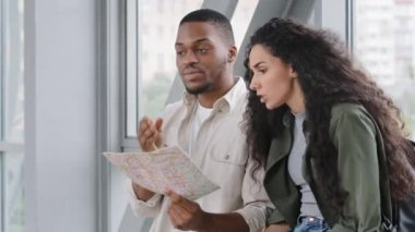 Çok ırklı çift yeni evli Afro-Amerikan erkek ve İspanyol kadın kavgası tren istasyonundaki havaalanı terminalinde oturup haritaya bakarak yeni ülke seyahatinde anlaşmazlık tartışması yapıyorlar.