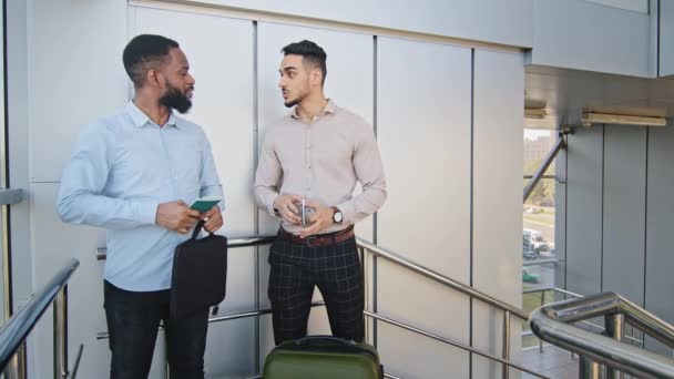 Twee multi-raciale zakenpartners collega 's Afro-Amerikaanse man en Spaanse man staan op het vliegveld met koffer en vliegtickets kijken naar polshorloge laat op de trap naar boven stormend om aan boord te gaan. — Stockvideo