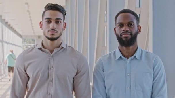 Retrato dos hombres serios socios de negocios multirraciales compañeros de trabajo hombres de negocios afroamericanos chico gerente y hombre hispano inversor de pie en el interior de la oficina posando en el pasillo mirando a la cámara — Vídeos de Stock