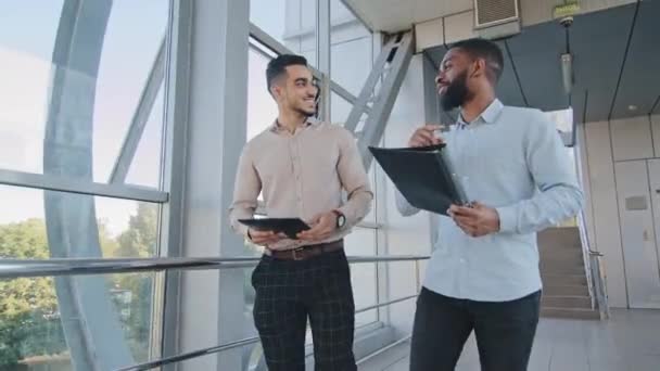 İki çok ırklı iş adamı girişimci yöneticiler işçiler Afrikalı Amerikalı patron ve İspanyol adam şirket ofisinde koridorda yürüyorlar ve proje iletişimini tartışıyorlar. — Stok video