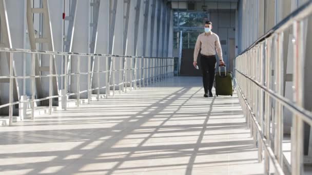 Hiszpan człowiek odnoszący sukcesy biznesmen pasażer w formalnych ubraniach nosi walizkę z bagażem nosi maskę twarzy od infekcji koronawirusa covid posiada paszport i bilety lotnicze idzie na lotnisko terminal — Wideo stockowe