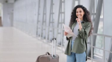 Genç, güzel esmer, İspanyol bir kadın elinde bavuluyla havaalanının haritasını tutuyor. Yol haritası arıyor. Fikri bulan kişi gülümseyen bir kadın turist buluyor.