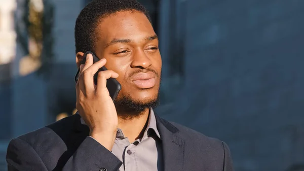 Serieuze gefocuste duizendjarige Afro-Amerikaanse zakenman buiten praten over de telefoon, jonge gemengde ras ondernemer spreken op mobiele telefoon, zakelijke problemen op te lossen. Mobiele professionele communicatie — Stockfoto