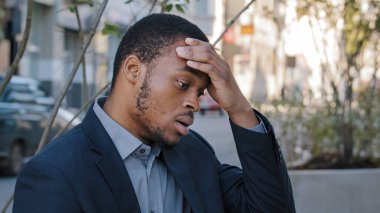 Stresli, genç, karışık ırk çalışanı bilgisayarın aşırı çalışması ya da sabit çalışma tarzı yüzünden acı çekiyor. Yorgun siyah adam, iş adamı açık havada işlerle boğuşuyor.