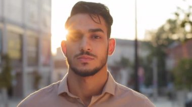 Portre erkek sakin ciddi yüz sokakta şehir güneş ışığı arka planında. Latin Arap sakallı adam başarılı bir iş adamı. Dışarıda duruyor ve günbatımında kameraya bakıyor.