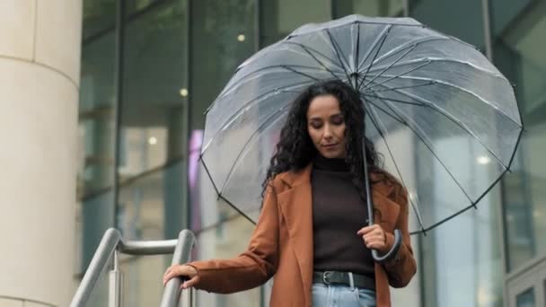 Piękna młoda dziewczyna biznes kobieta brunetka pani z przezroczystym parasolem spaceru schodami w pobliżu biurowca centrum handlowego firma idzie pozostawia sklep w deszczu deszczowa pogoda ulewa idzie sam — Wideo stockowe